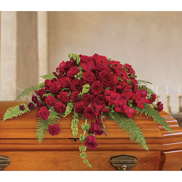 Decorative arrangement of red flowers on wooden casket against neutral background