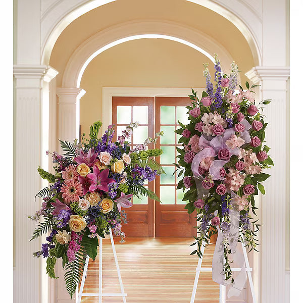 Two floral arrangements on stands in a room with an archway and wooden door.