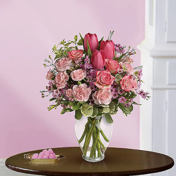 Pink flower bouquet in clear vase on wooden table.