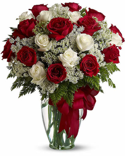 Bouquet of red and white roses in a clear vase with a red bow on a white background