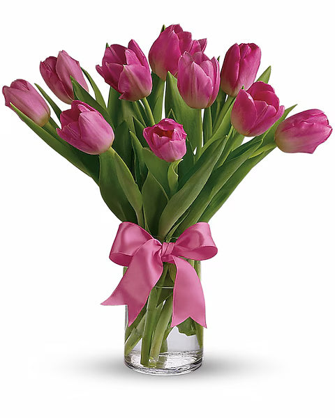 Bouquet of pink tulips in a clear vase with a pink ribbon on a white background