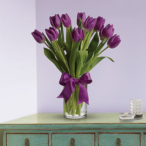 Bouquet of tulips in a clear vase on a reflective surface.
