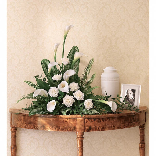 Elegant tabletop arrangement of flowers with urn and picture frame against beige wall