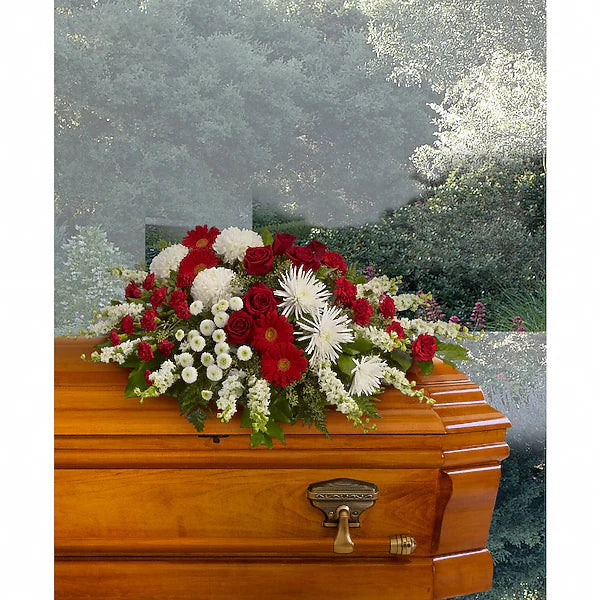 Vibrant red, white, and green floral arrangement on wooden casket outdoors