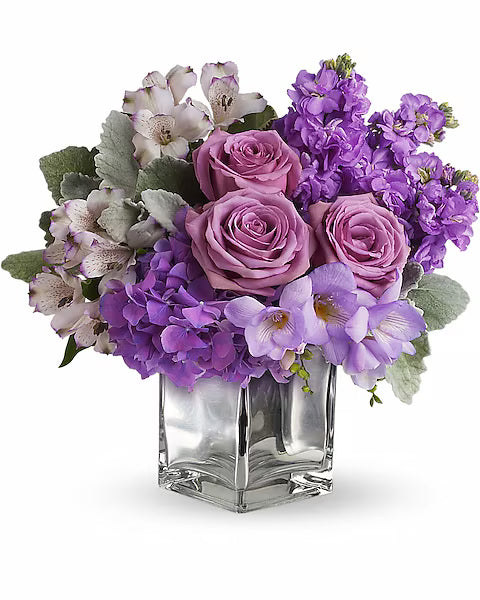 Stylish floral arrangement in glass vase featuring purple and pink flowers.