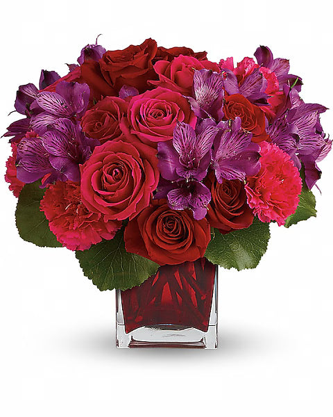 Bouquet of red and pink roses with purple flowers in a clear red vase