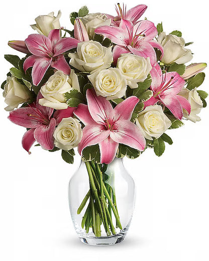 Bouquet of pink lilies and white roses in a clear vase on a white background